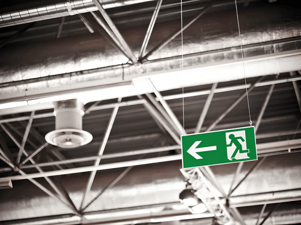 Emergency exit sign with left-pointing arrow inside an industrial building